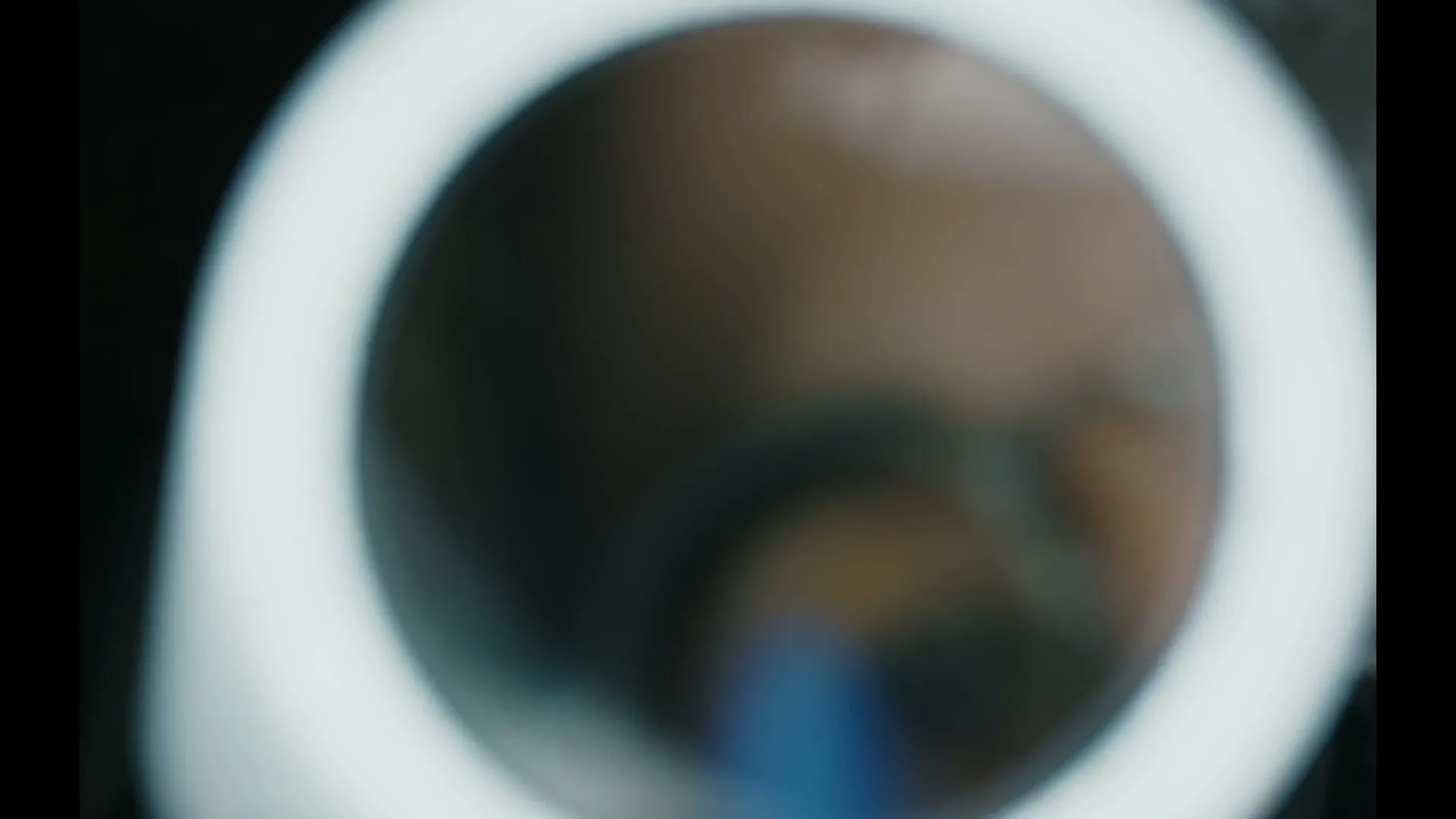 A person with glasses is seen through a circular light, looking intently at something off-screen in a close-up shot.