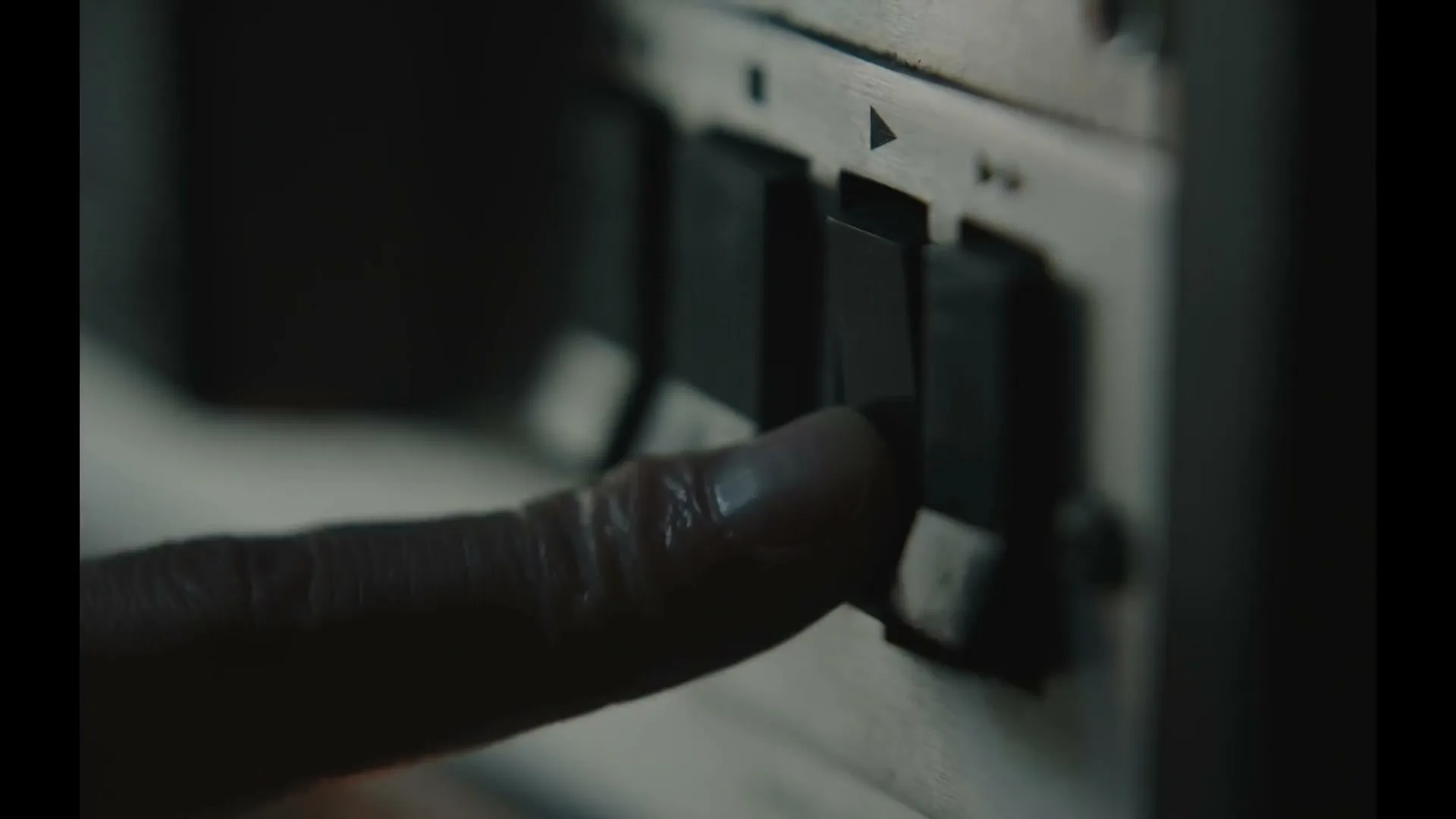 A person's finger presses a black button on an old-fashioned audio device, activating it in a dimly lit interior.
