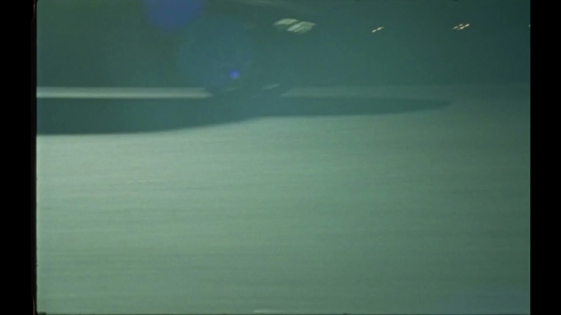 A dark, blurry shot of a car driving at night, with headlights visible and a lens flare.