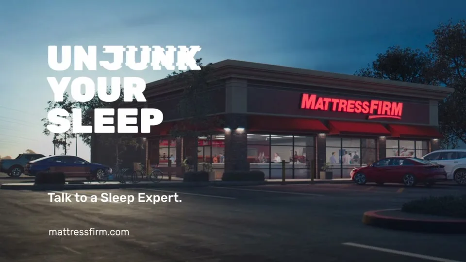 A wide shot of a Mattress Firm store at dusk, with cars parked outside and people visible inside, accompanied by on-screen text.