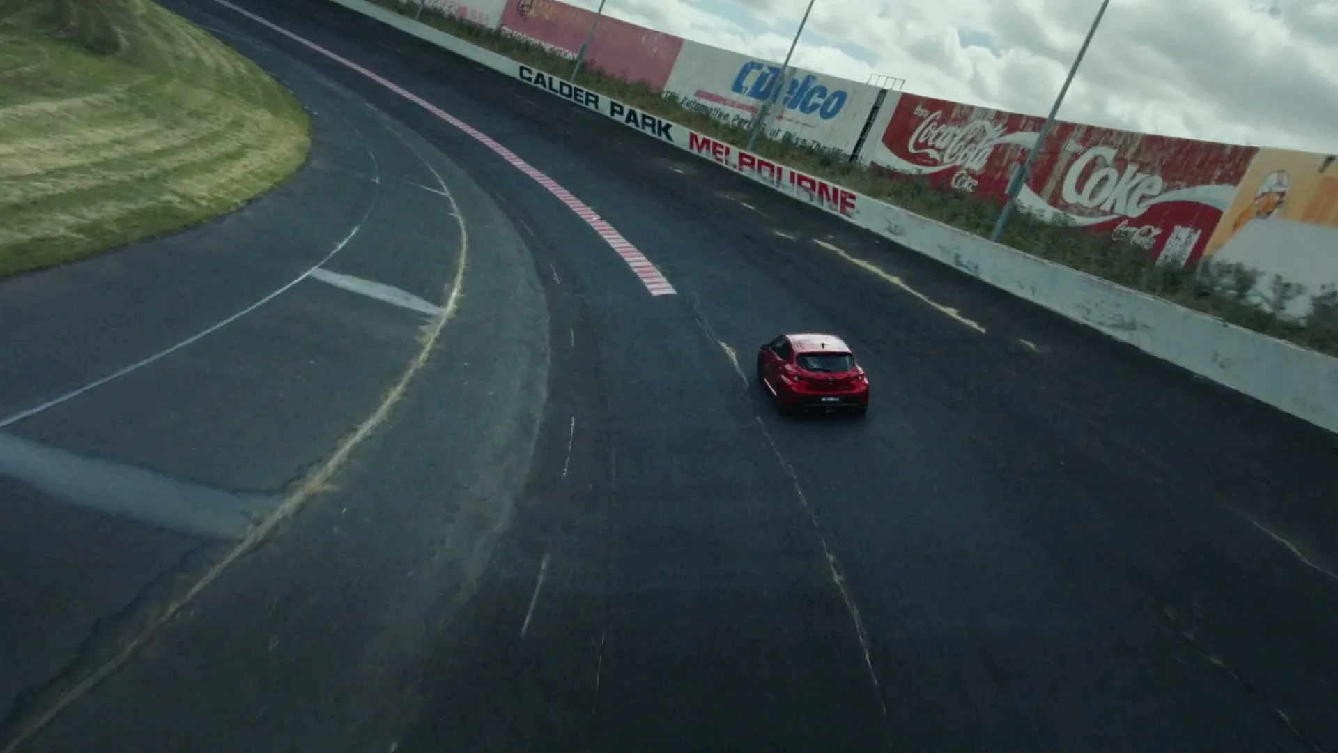 A red Toyota GR Yaris drives on a race track, leaving a trail of "MADE" text behind it, under a cloudy sky.