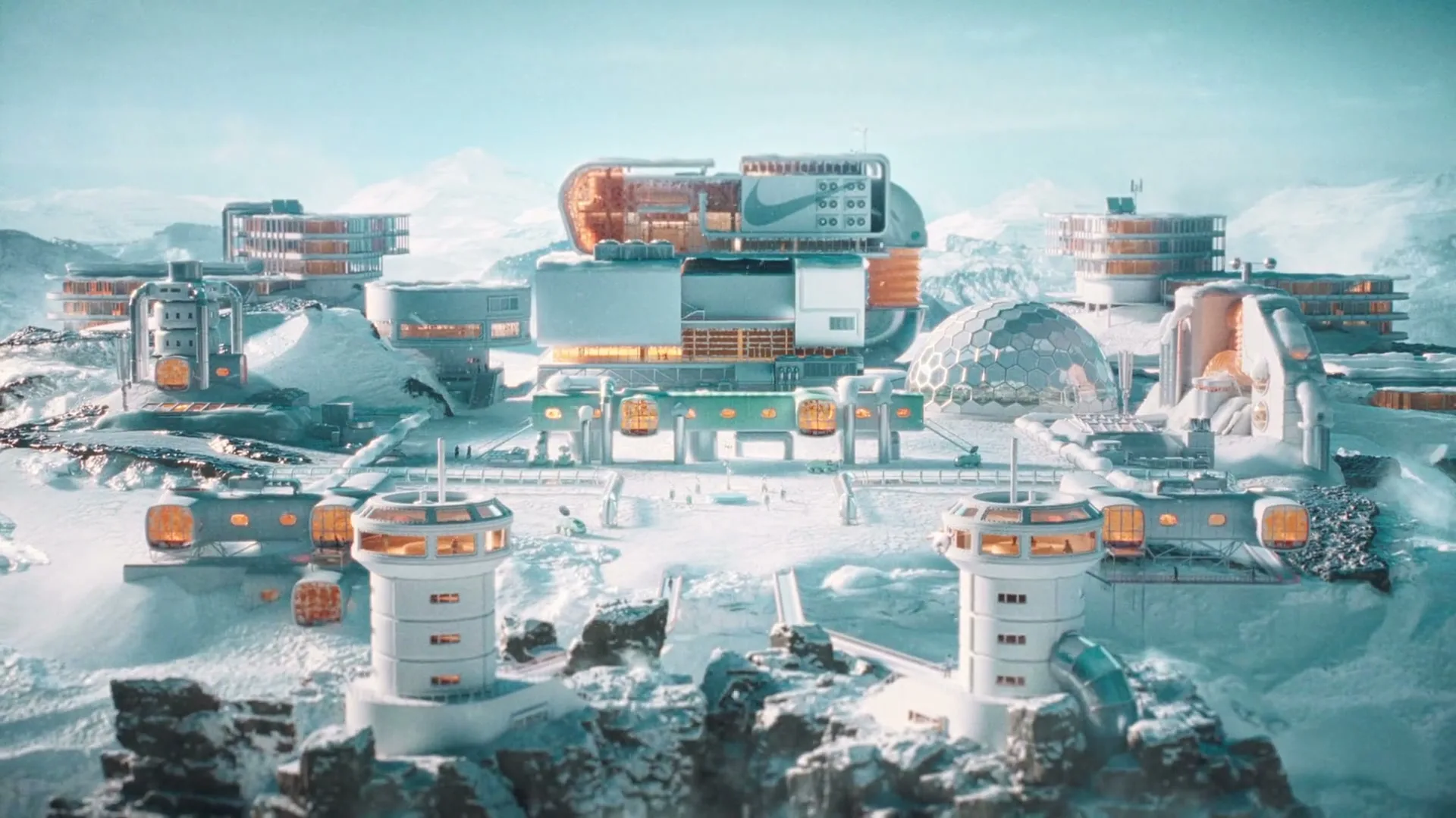 An extreme wide shot shows a futuristic, sprawling research base nestled in a vast, snow-covered mountain range under a bright, clear sky.