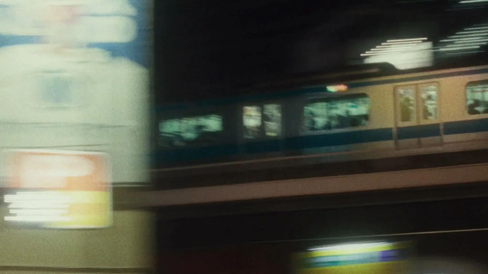 A blurry shot of a subway train with passengers inside, speeding past a platform at night in a city.