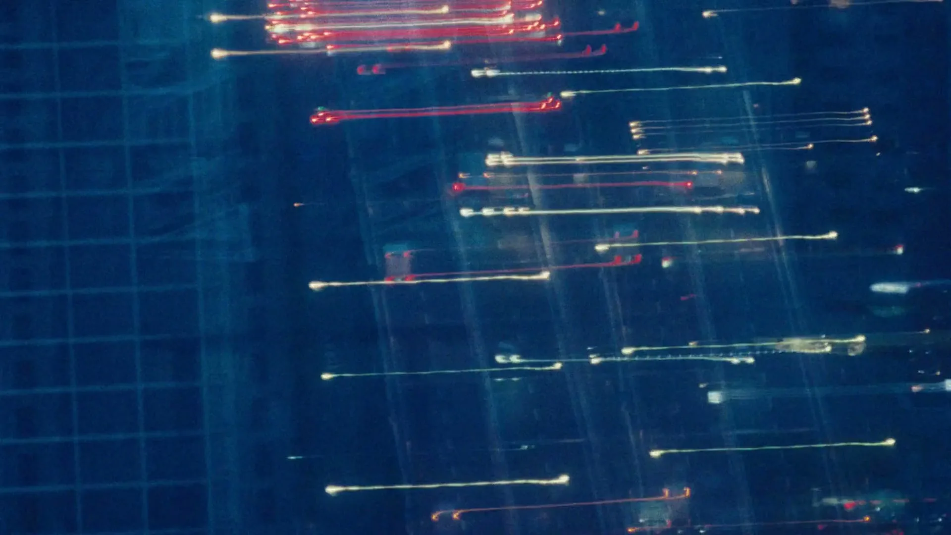 An abstract shot of blurred red and white light trails against a dark blue background, resembling car lights at night.
