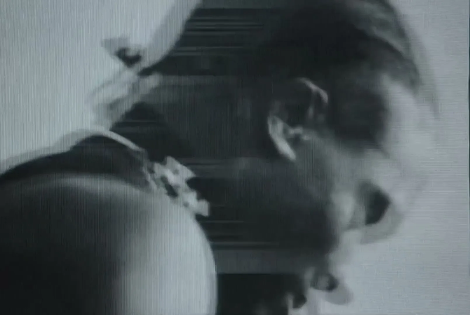 A black and white, grainy, extreme closeup shot of a person's head and shoulder, looking down, with motion blur.