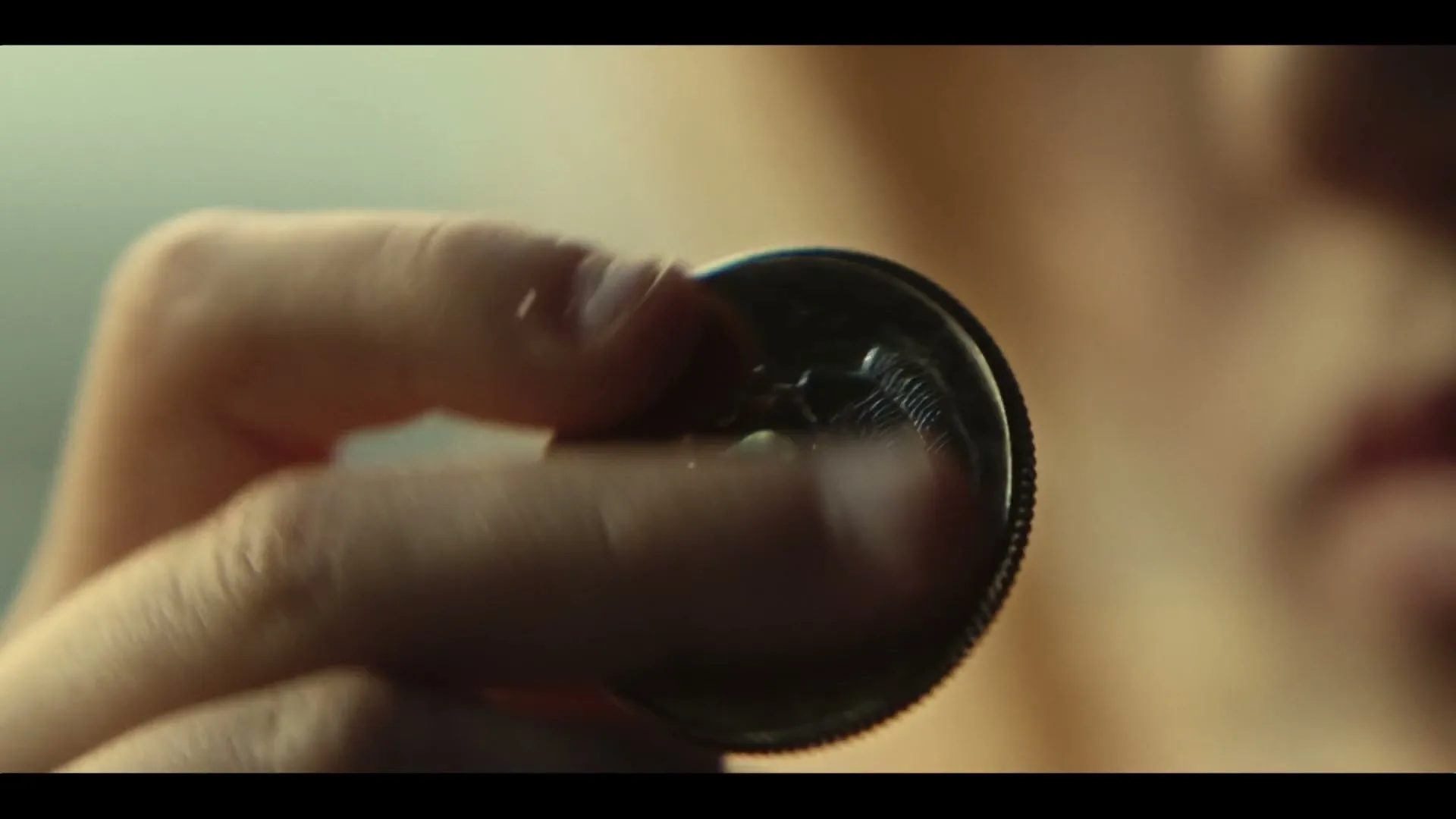 A person's hand holds and flips a coin, with their face slightly visible in the blurred background.