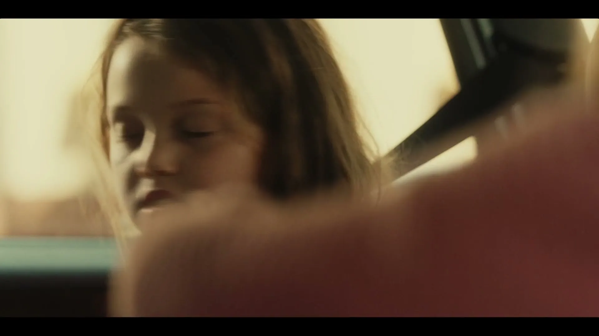 A young girl with long brown hair and blue eyes looks intently at someone off-screen, her expression curious and slightly open-mouthed.