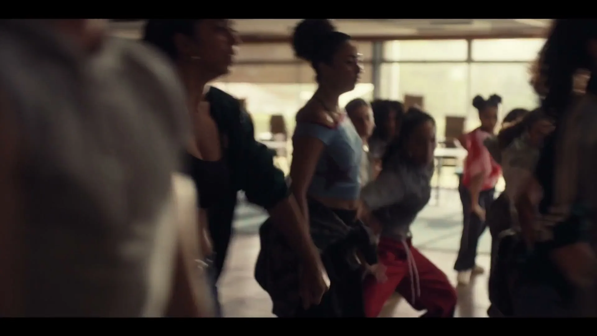 A diverse group of young women in casual attire are seen from the waist up, dancing in a brightly lit studio.