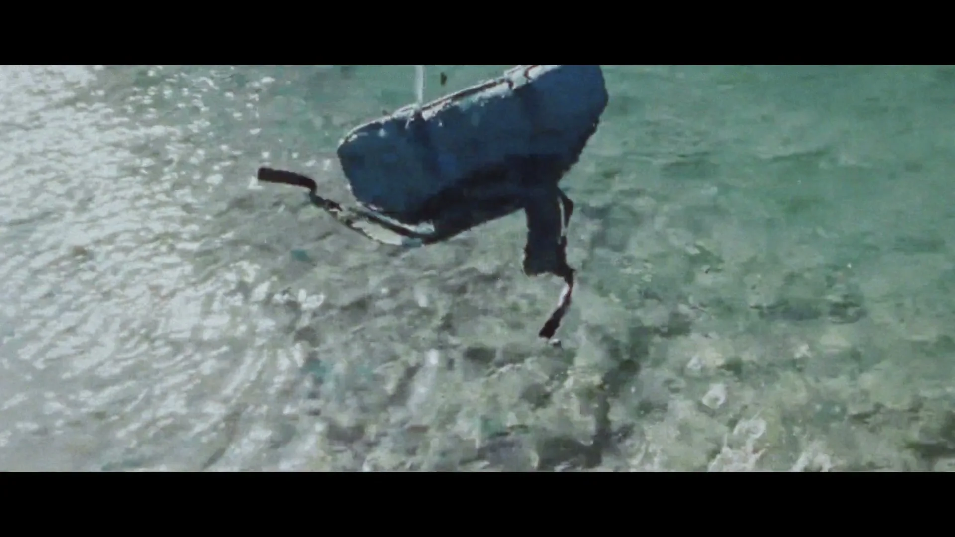 A person's hand points at a map, then a YETI cooler is seen submerged in clear water, and finally, it's pulled out, covered in mud.