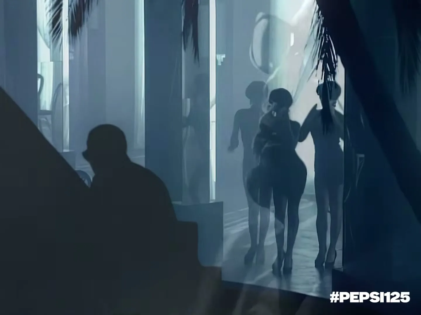 A man in silhouette watches three women in dresses dancing in a club with palm trees and blue lighting.