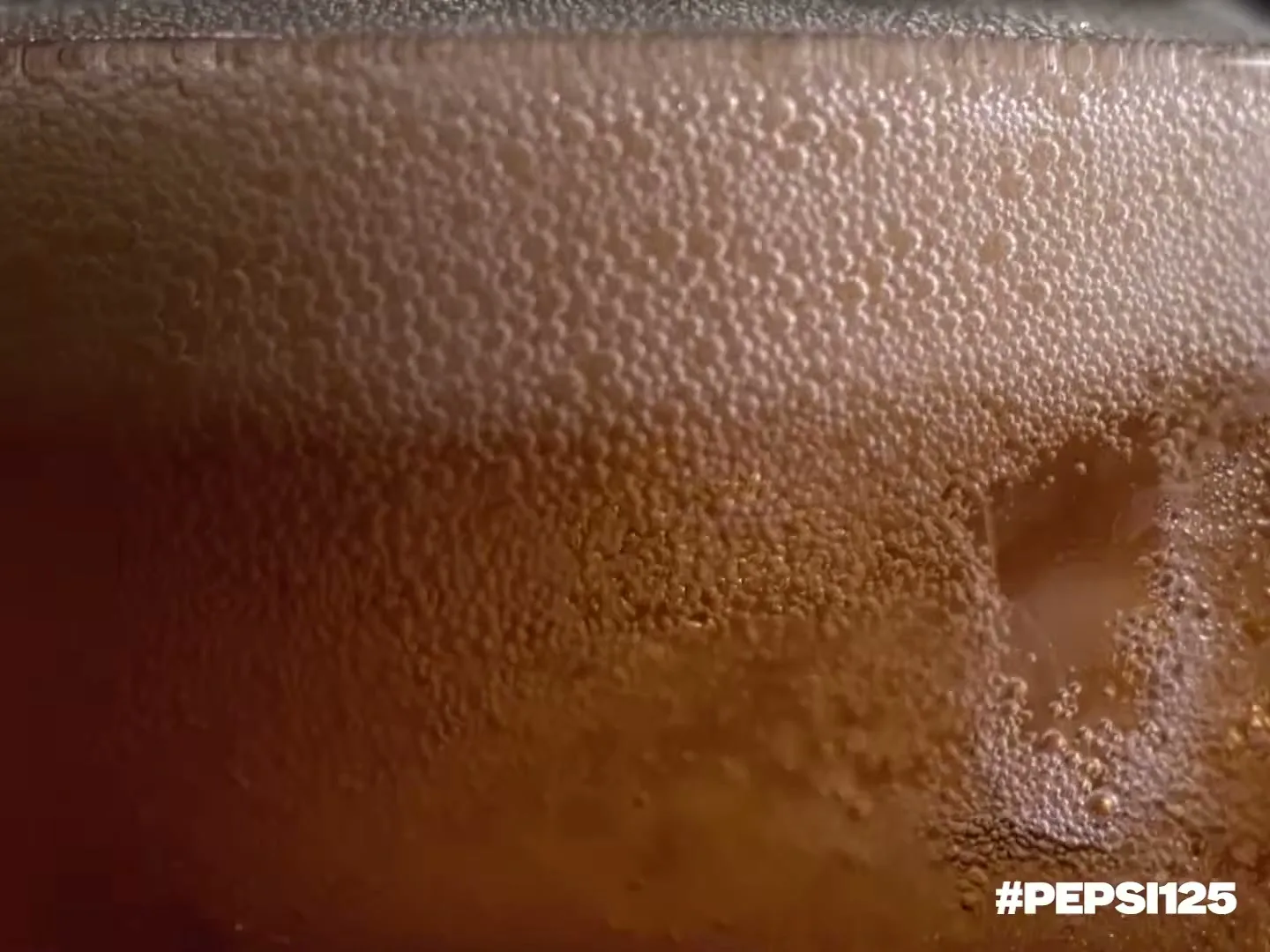 A close-up shot of a glass of Pepsi, showing the carbonated bubbles and foam, with the hashtag #PEPSI125 visible.