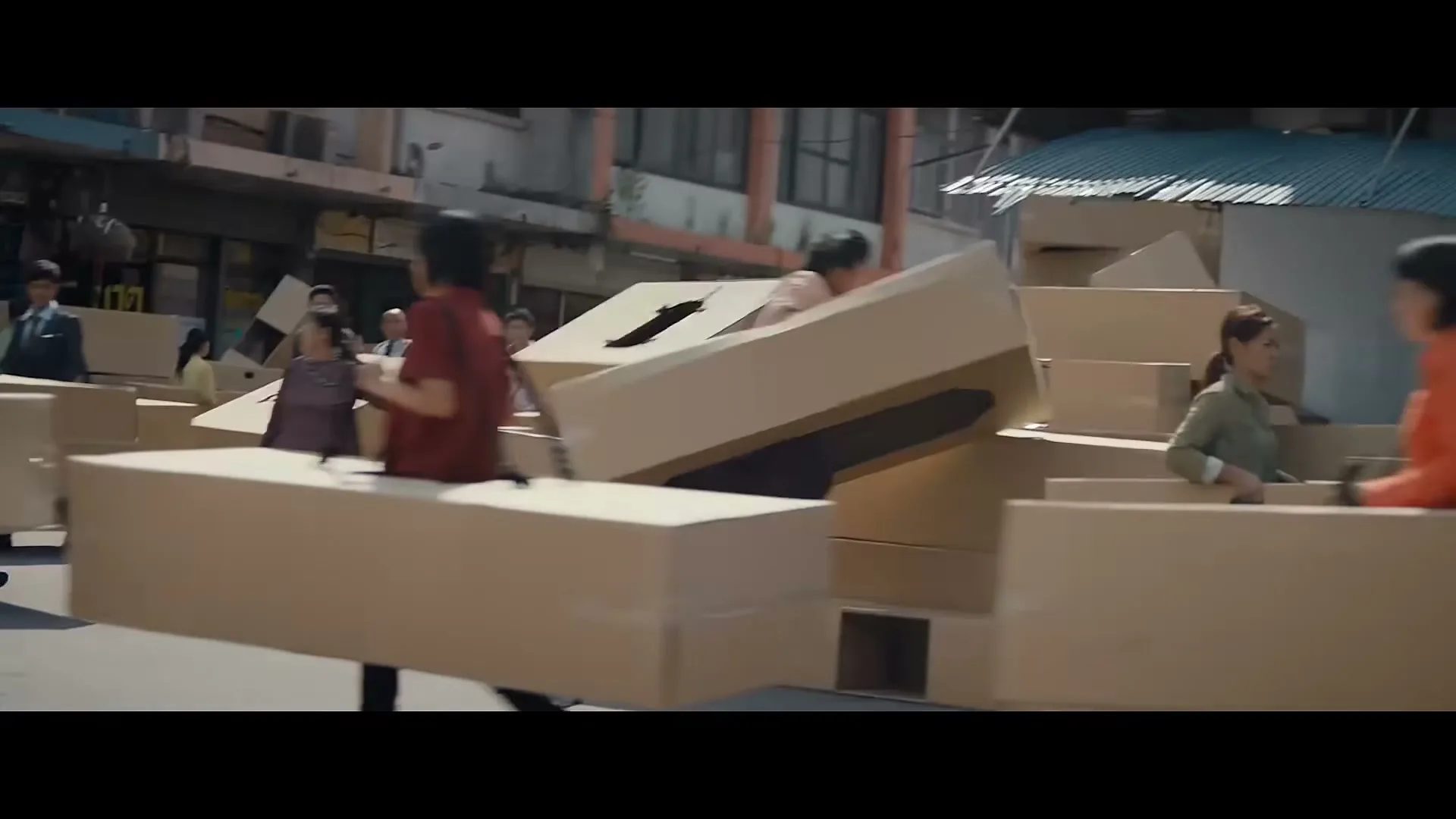 A man in a pink shirt and striped tie, surrounded by people wearing cardboard boxes, struggles to move forward on a busy street.