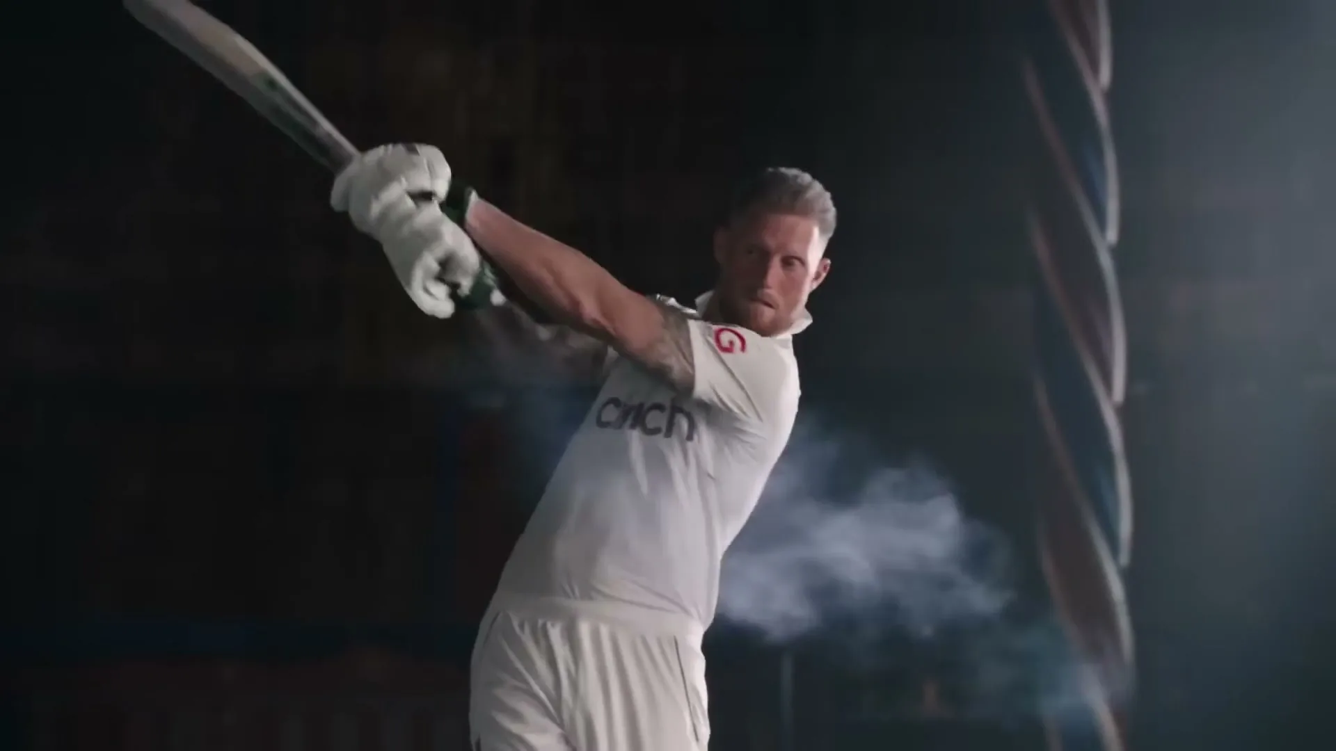A male cricketer in white uniform swings a bat, hitting a ball that creates a puff of smoke in a dark, dramatic setting.