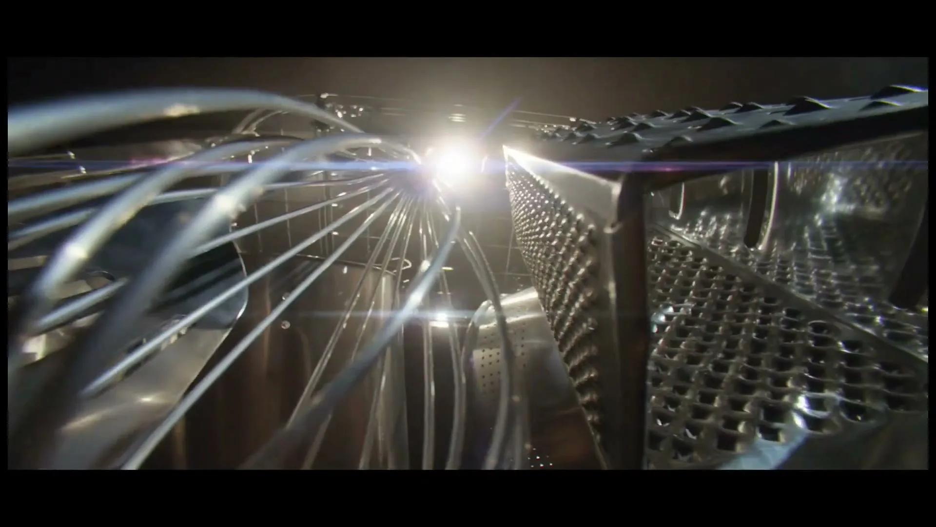 A close-up shot of kitchen utensils, including a whisk and a grater, with a bright light source in the background, creating a lens flare.