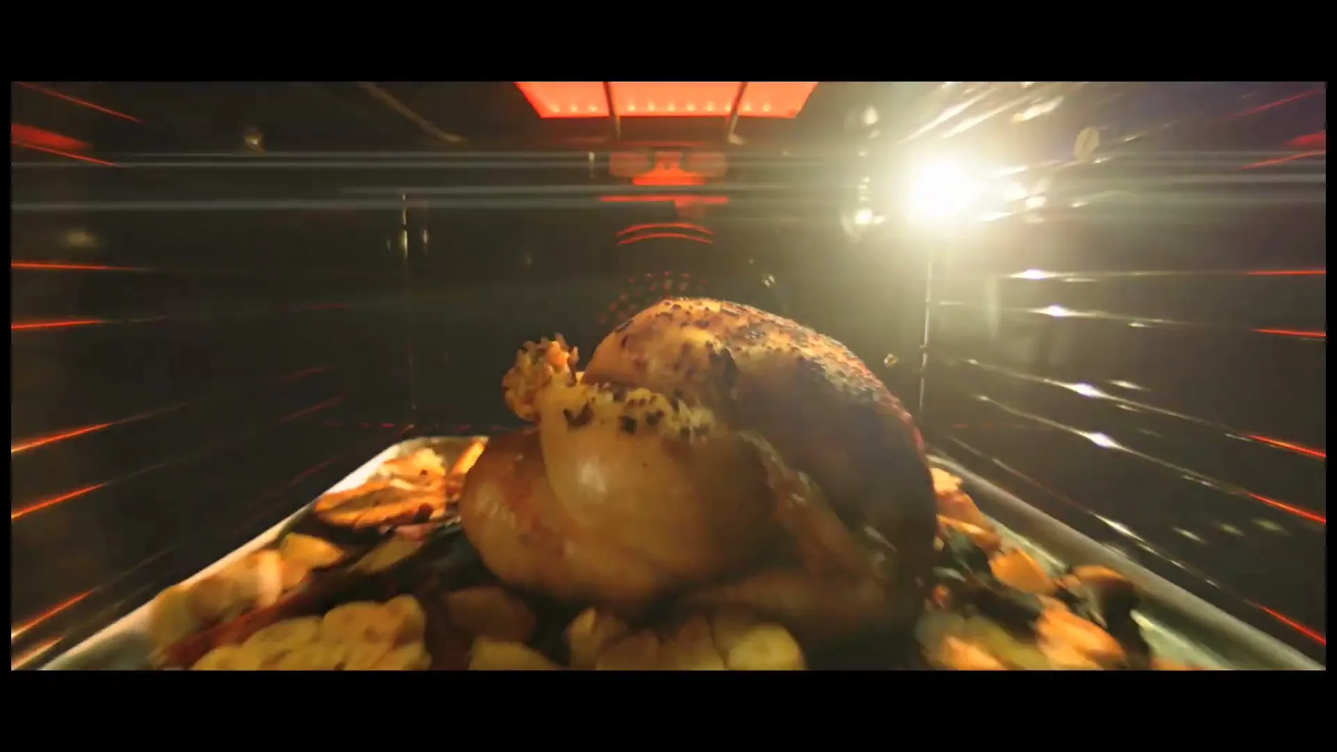 A golden-brown roasted chicken on a tray with potatoes and lemons is seen inside a dark oven, with a bright light source on the right.