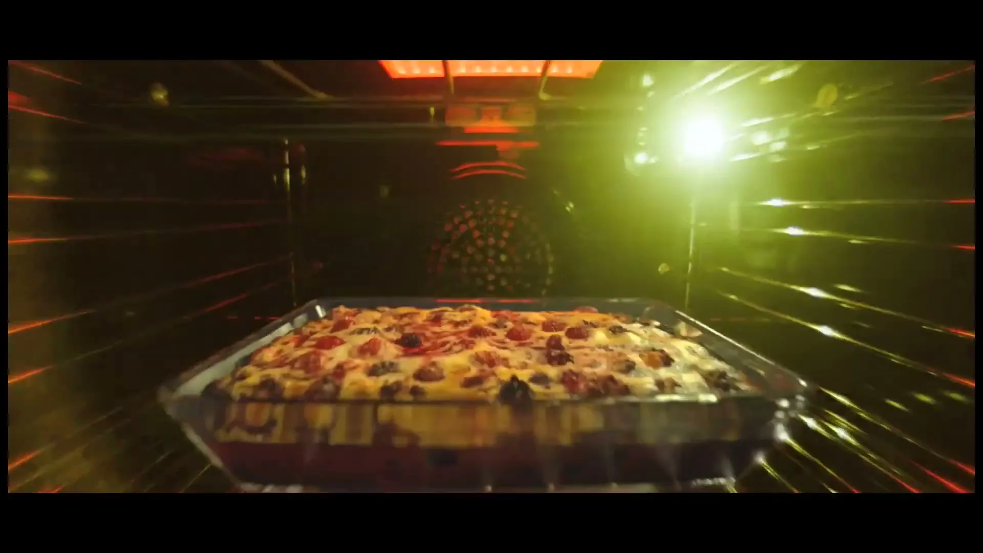 A glass baking dish filled with a dessert, possibly a crumble or cobbler, bakes inside a dark oven with glowing red heating elements.