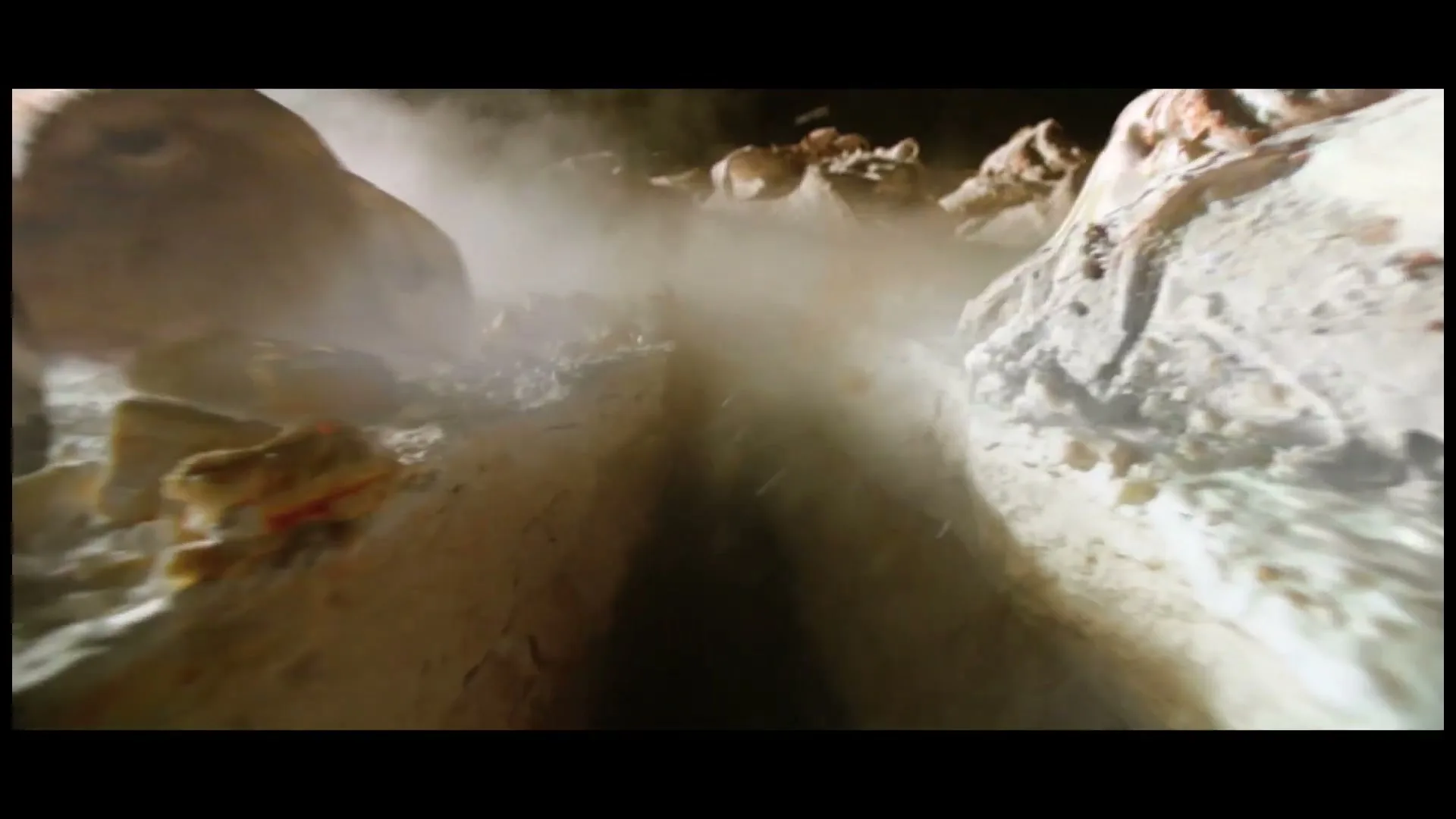 A close-up shot shows a narrow, dark crevice with rough, textured walls, as dust and debris fall into the abyss.