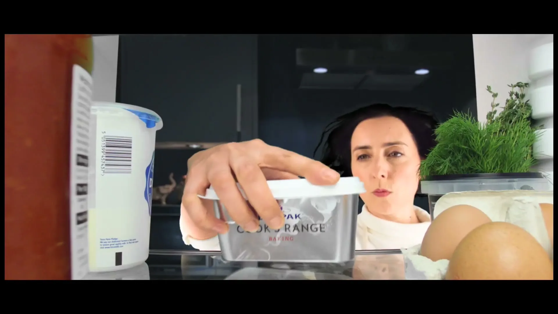 A woman with dark hair and a white top reaches into a refrigerator, grabbing a tub of Lurpak Cook's Range Baking butter.