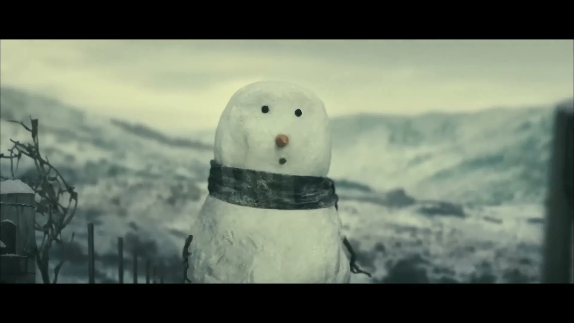 A snowman with a scarf stands in a snowy, desolate landscape with hills in the background, looking surprised.