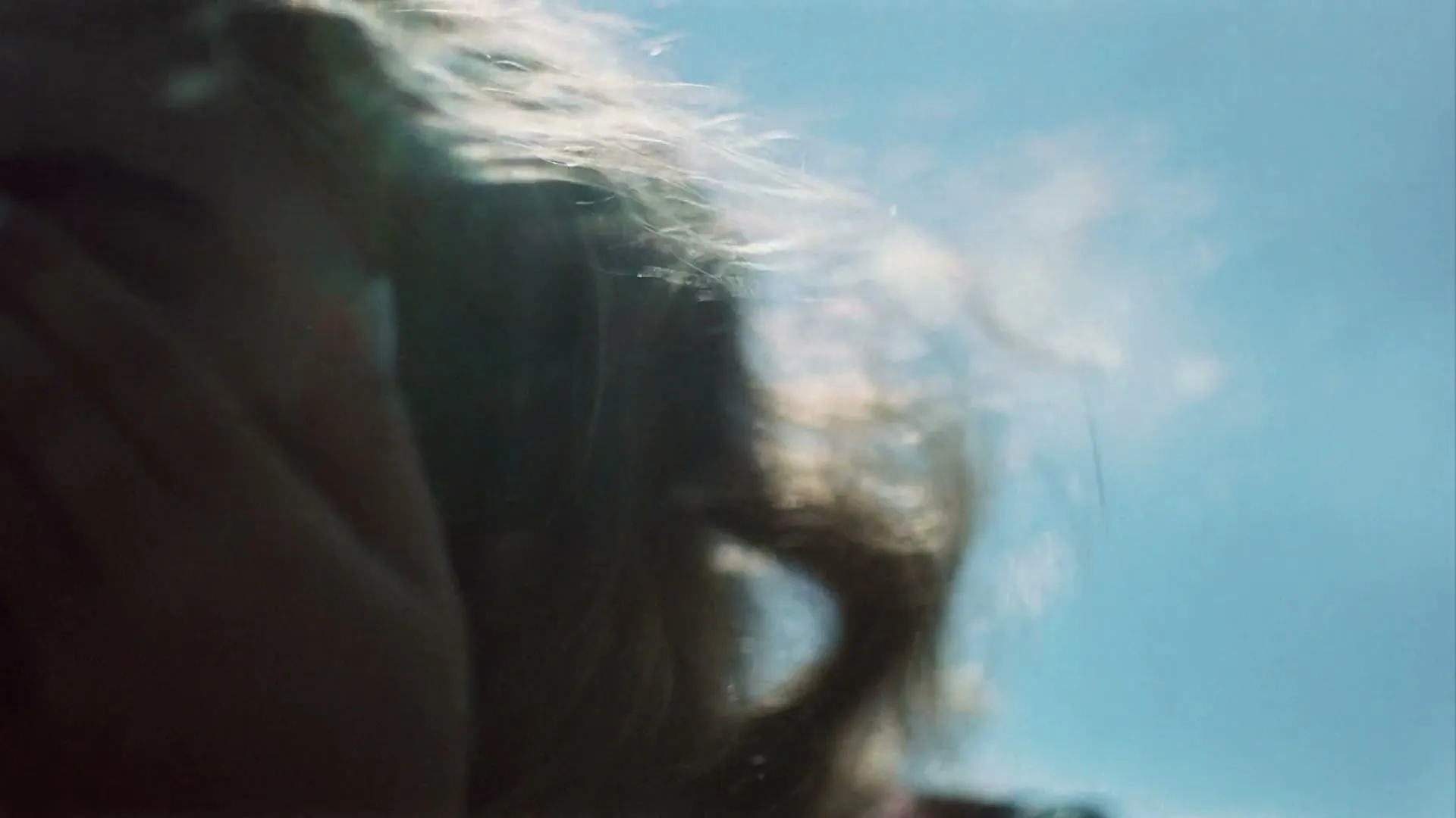 A blurry, extreme closeup of a person's head and hair, with bright sunlight and a blue sky in the background.