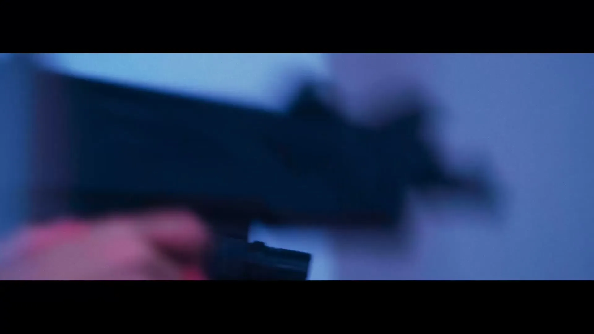 A person's hand with pink nail polish holds a black toy gun, moving it into frame against a blurry blue background.