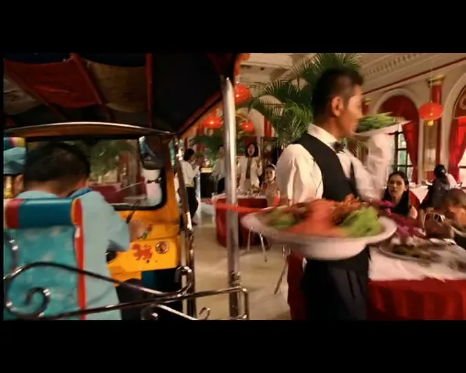 A tuk-tuk drives through a fancy restaurant, passing a waiter carrying a large platter of food, as diners look on.