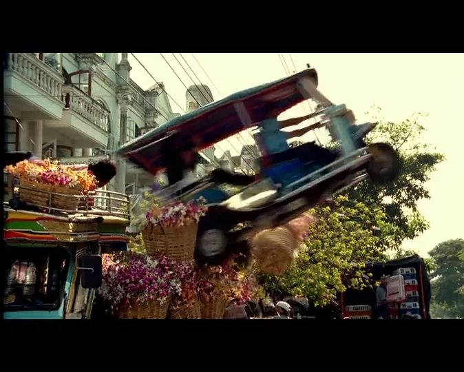 A tuk-tuk crashes into a flower truck, sending flowers flying into the air on a busy street in a city.