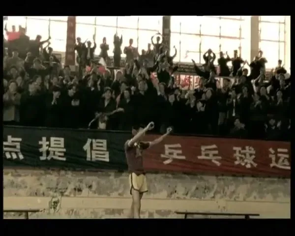 A male athlete in a maroon shirt and yellow shorts celebrates a victory in front of a cheering crowd in a stadium.