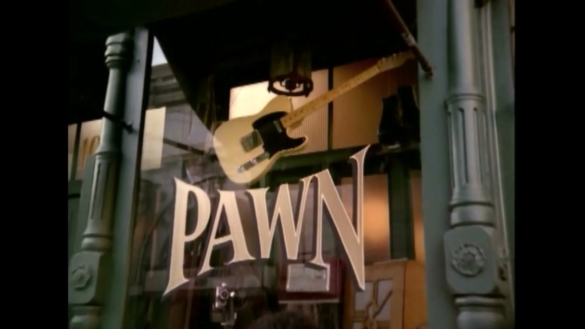A close-up shot of a pawn shop window with a guitar and the word "PAWN" visible, as a person's head is seen in the reflection.