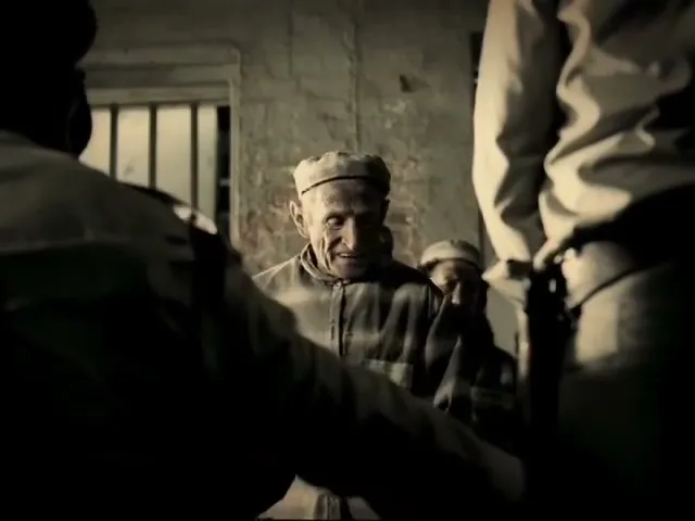 An old male prisoner in striped uniform smiles at a guard in a prison hallway, while other prisoners stand behind him.