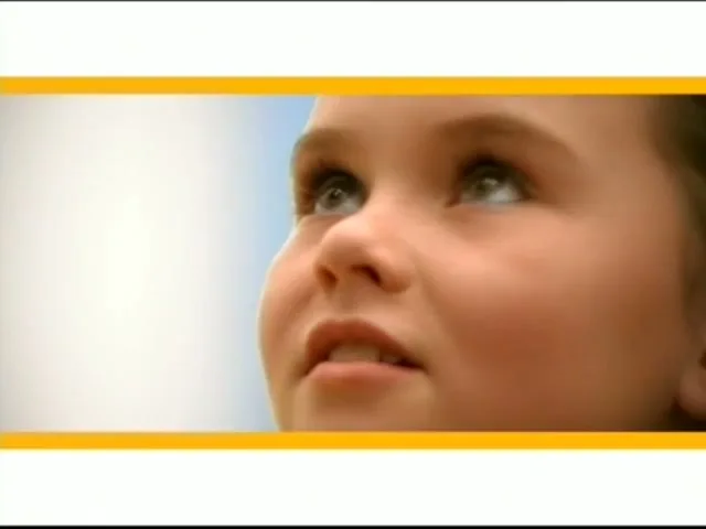 A young girl with light brown hair looks up with a curious expression, her face illuminated by natural light against a bright, slightly blurred background.