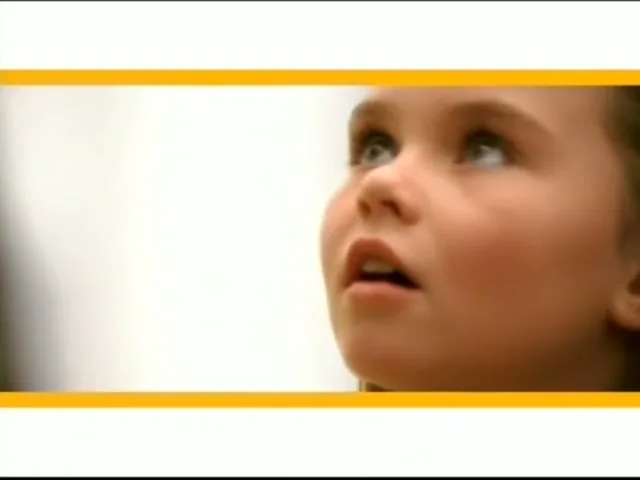 A young girl with brown hair looks up with an open mouth, her face illuminated by bright light.