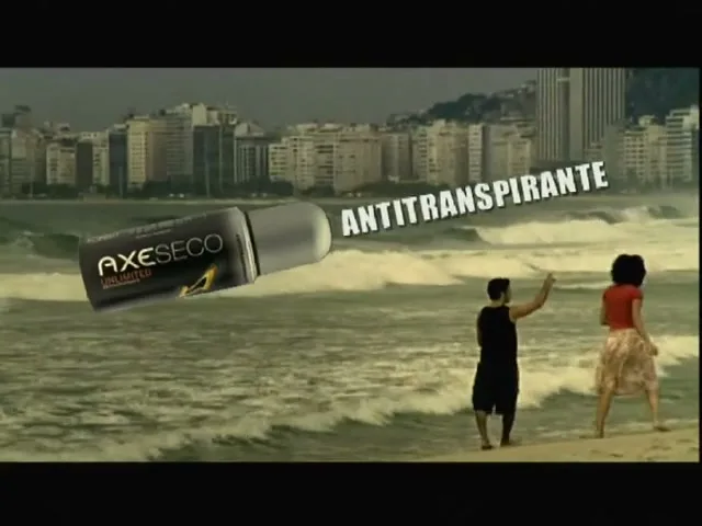 A man and a woman stand on a beach with a city skyline in the background, as a large Axe deodorant product and text float in the air.