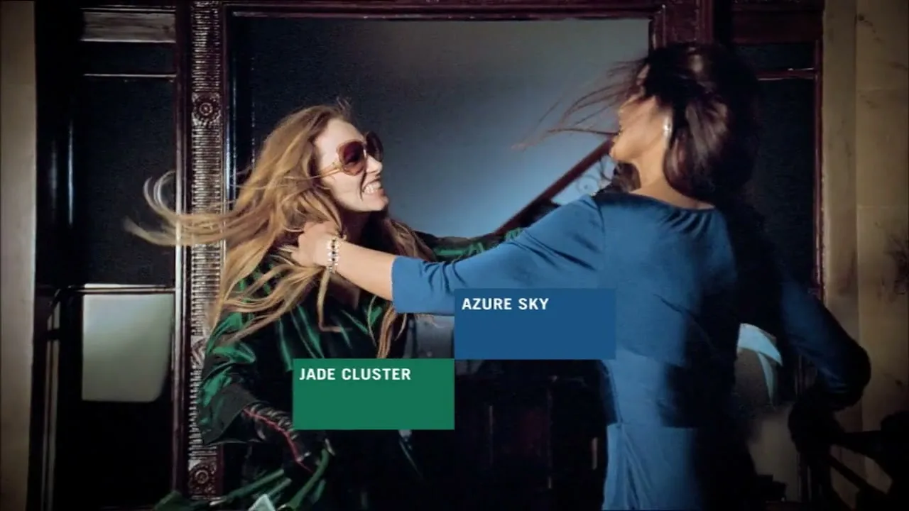 Two women, one in a green dress and the other in a blue dress, are fighting over a green handbag in a luxurious interior with statues and ornate furniture.