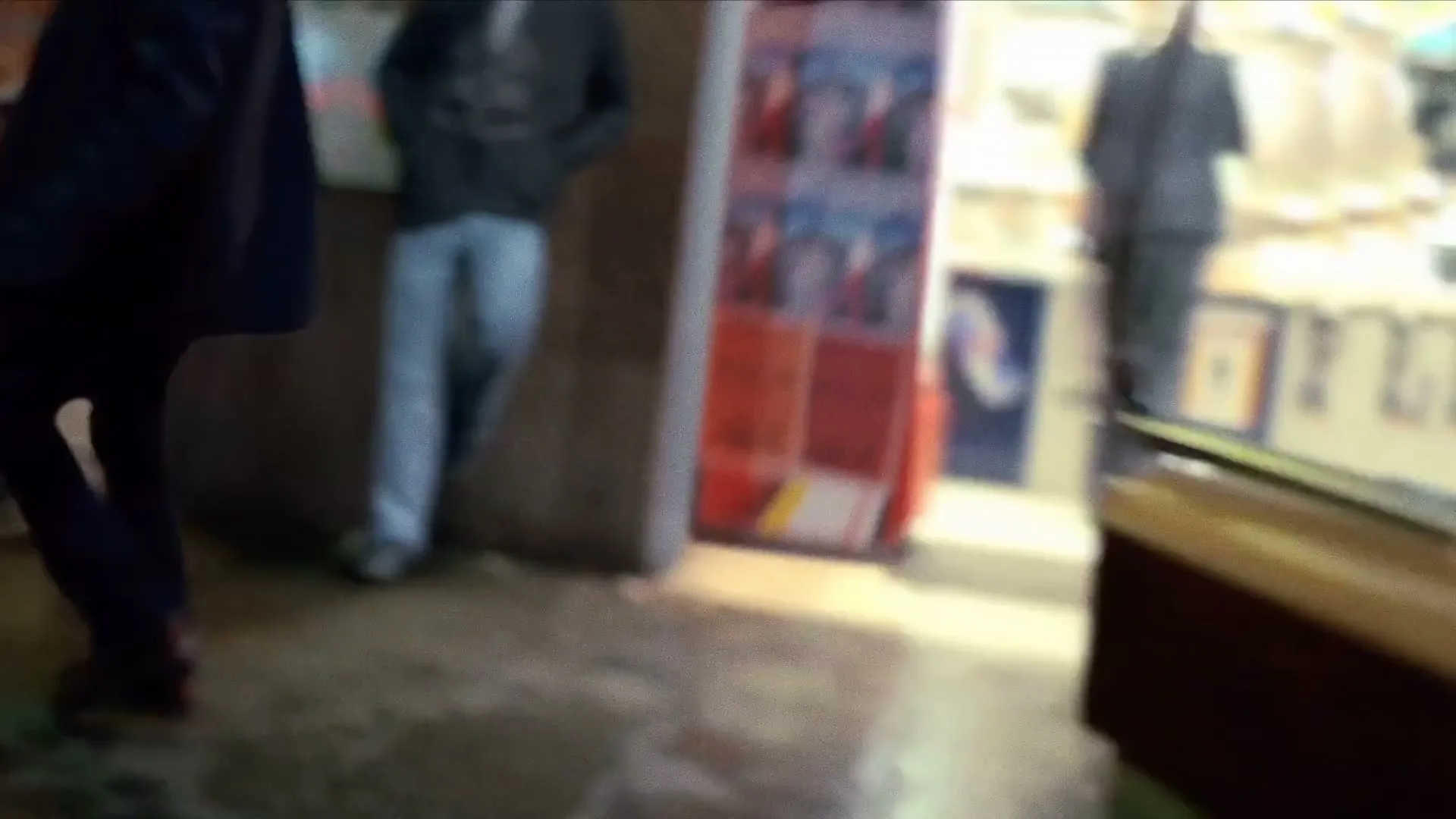 A blurry shot of a person's arm reaching out, with other blurry figures in the background of a brightly lit interior.