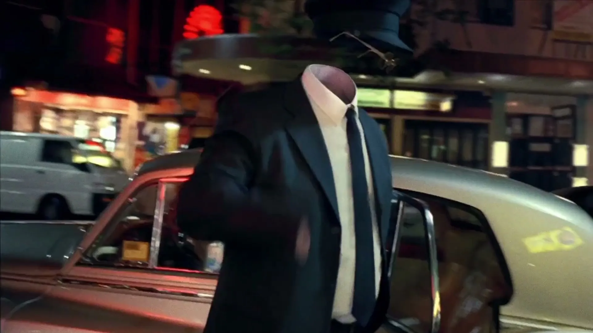 An invisible man in a suit and tie exits a vintage car on a busy city street at night, with neon lights reflecting on the wet pavement.