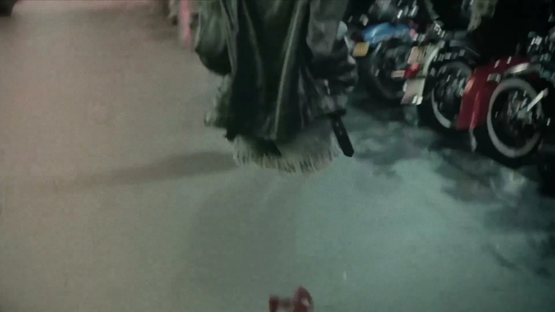 An invisible person in a studded leather jacket walks past motorcycles on a city street at night, with red high heels on the ground.