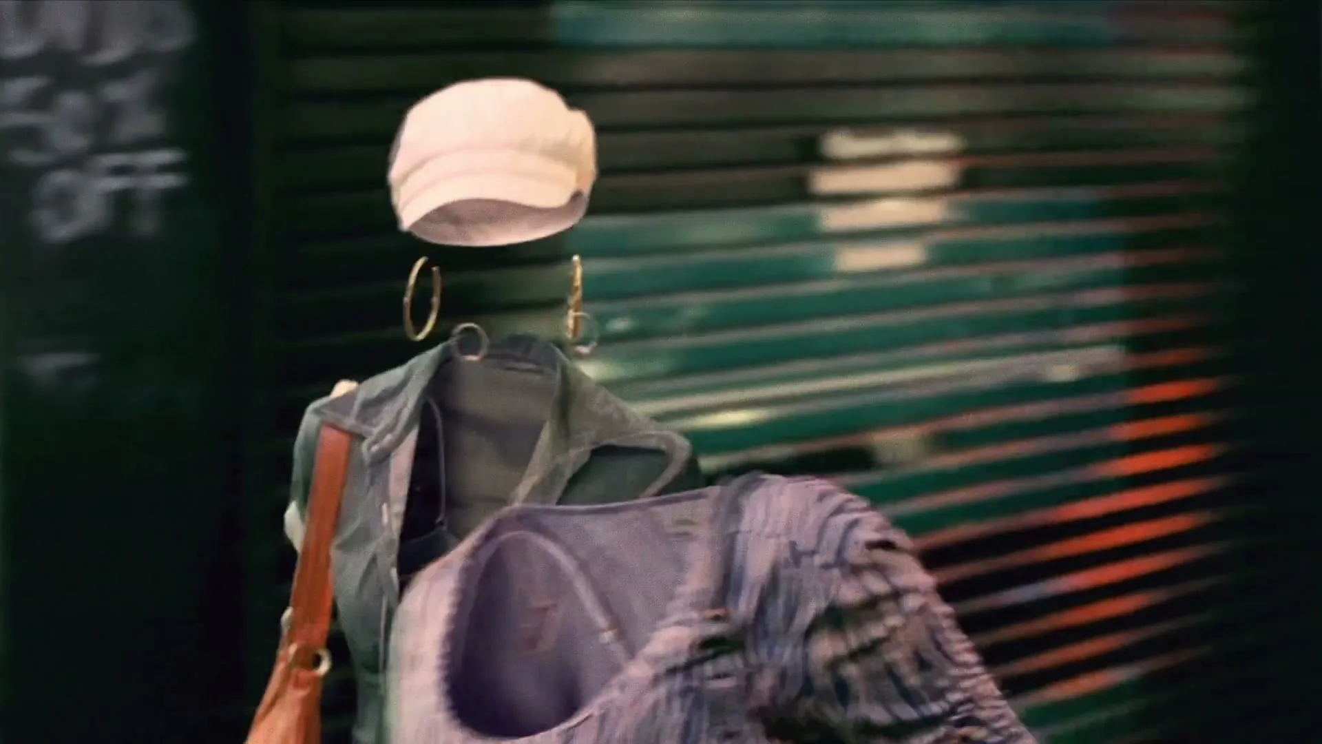 Two sets of clothes, seemingly worn by invisible people, walk down a narrow, dark city alley past closed storefronts.
