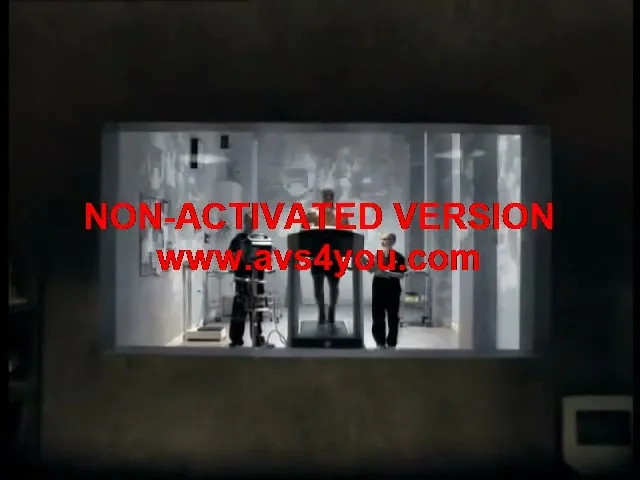 A male athlete runs on a treadmill in a glass chamber, observed by two scientists in a dimly lit lab.