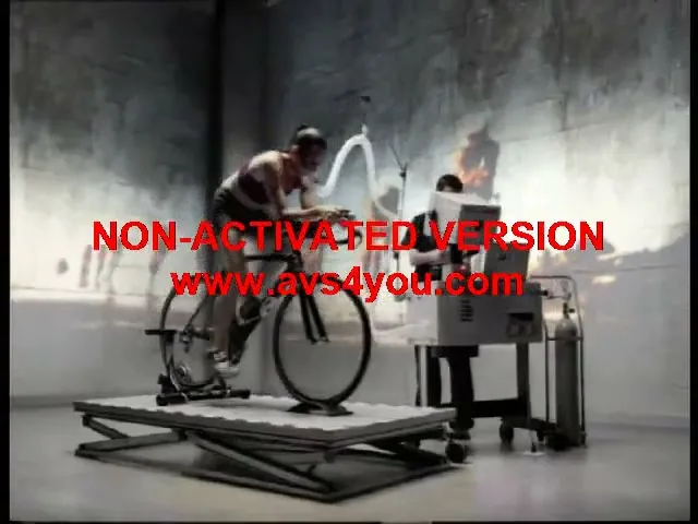 A male athlete in a tank top and shorts cycles on a stationary bike while connected to scientific equipment in a lab, with a scientist observing.