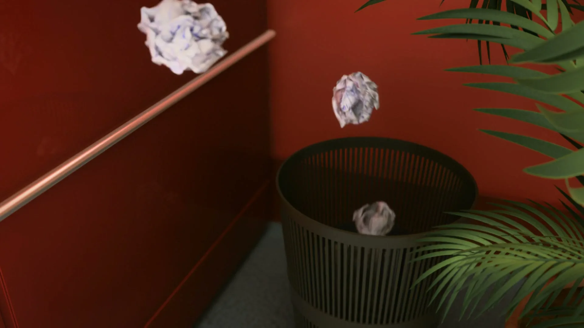 Crumpled pieces of paper magically fly into a trash can in a red-walled office corner with a green plant.