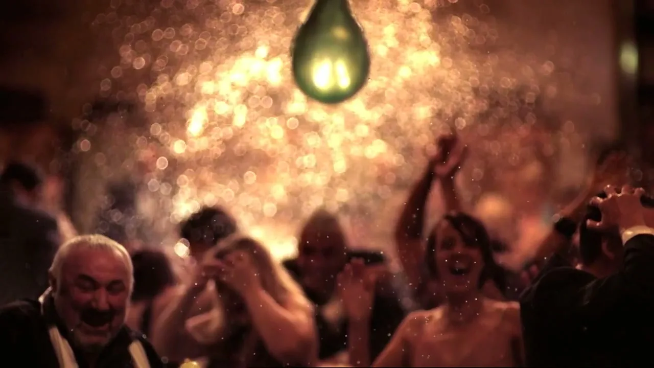 A diverse group of people, some with wet hair, are laughing and cheering as water droplets fall around them in a dimly lit, festive interior.
