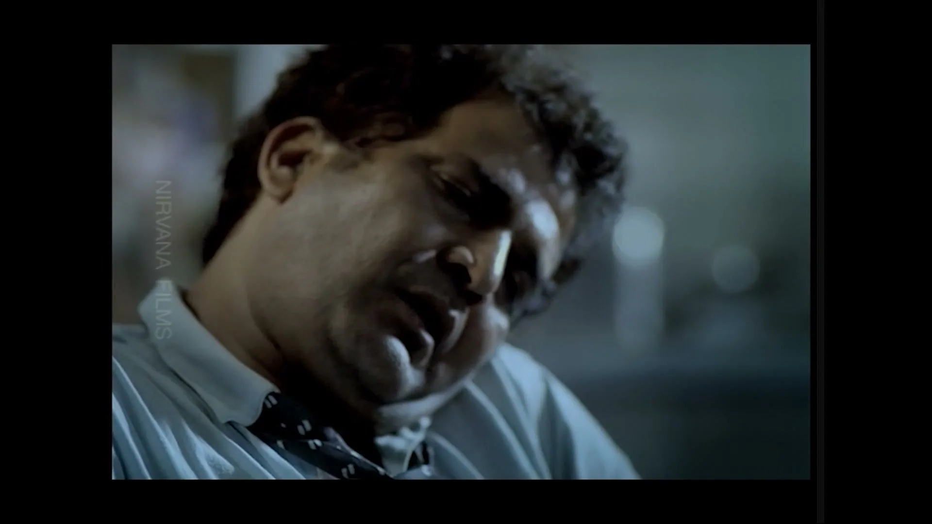 A man with dark, curly hair and a light blue shirt with a dark tie is seen in a medium closeup, looking distressed and sweating.