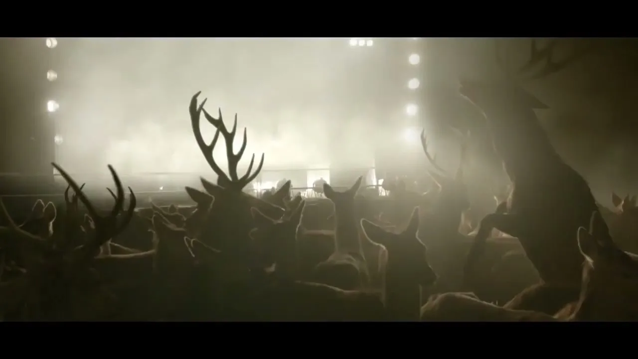 A herd of deer, some with large antlers, are silhouetted against bright stadium lights and smoke, appearing to be in a large arena.