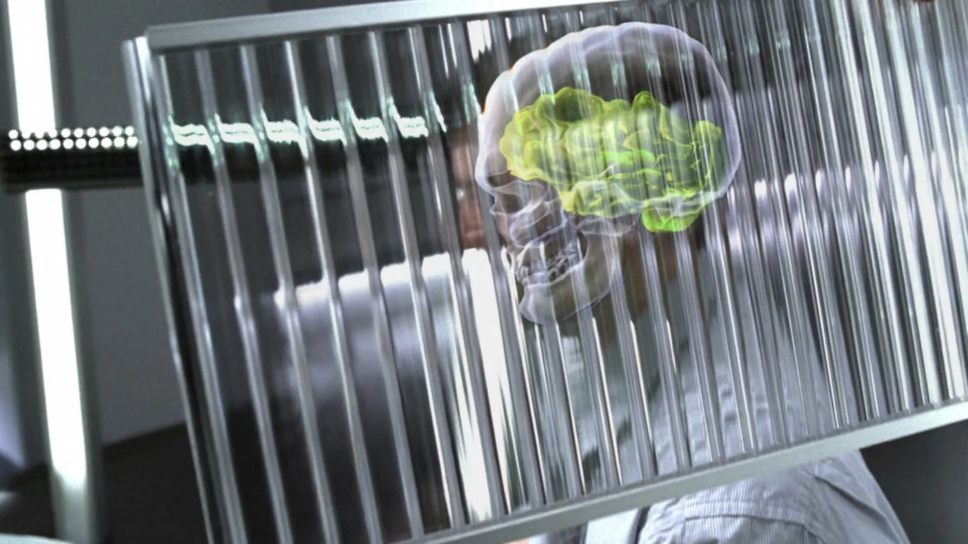 A man in a light blue shirt and tie sits at a desk, laughing, as a transparent grid with a glowing brain graphic is placed in front of his head.