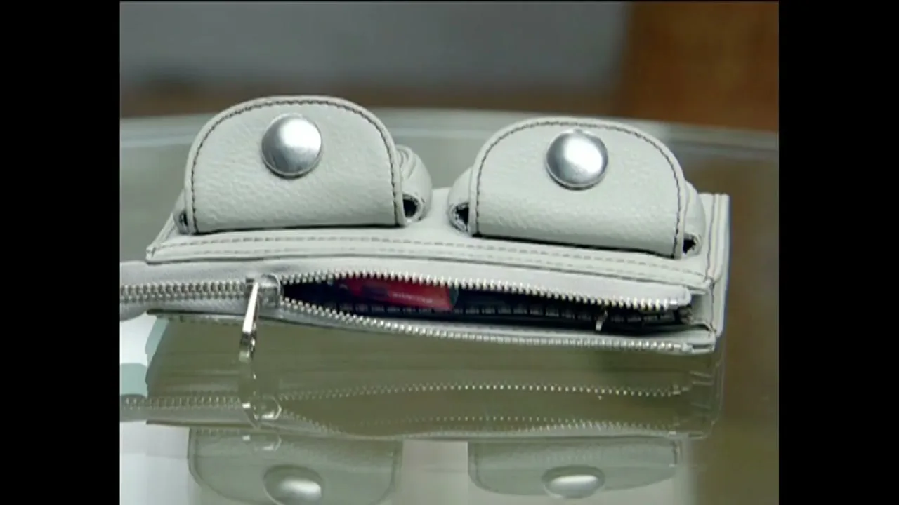 A light grey wallet with two buttoned pockets and a partially unzipped main compartment sits on a reflective surface, revealing a red item inside.