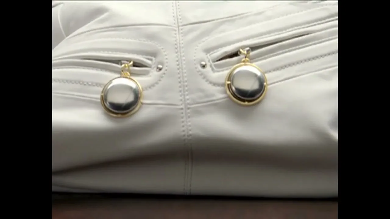 A pair of white leather pants with two shiny, round, gold-rimmed objects hanging from the back pockets, possibly decorative or functional.