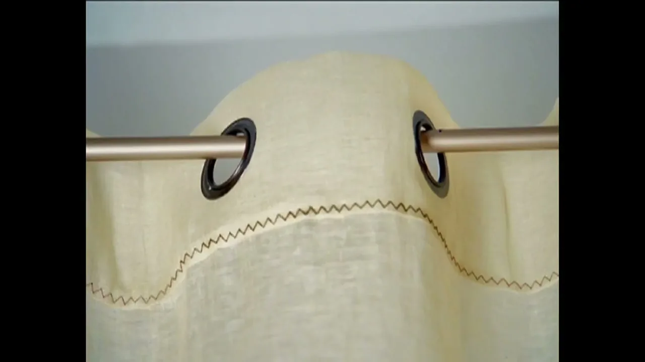 A close-up shot of a light-colored curtain with grommets on a rod, with a white wall in the background.