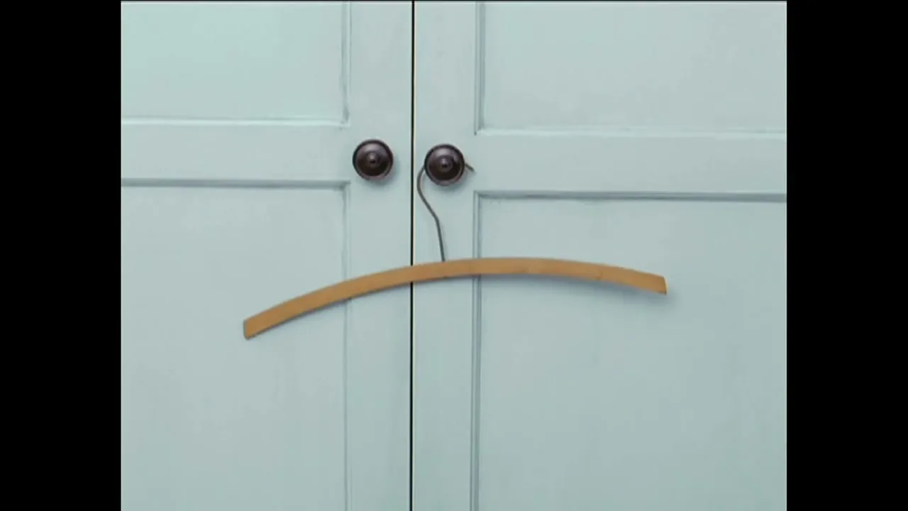 A wooden clothes hanger hangs on two light blue closet doors, forming a sad face with the door handles as eyes.