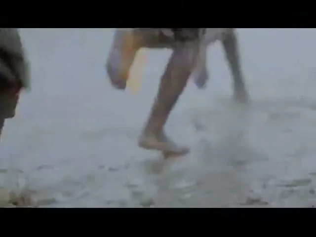 A group of children run barefoot through a muddy field, their legs and feet covered in dirt, during the day.